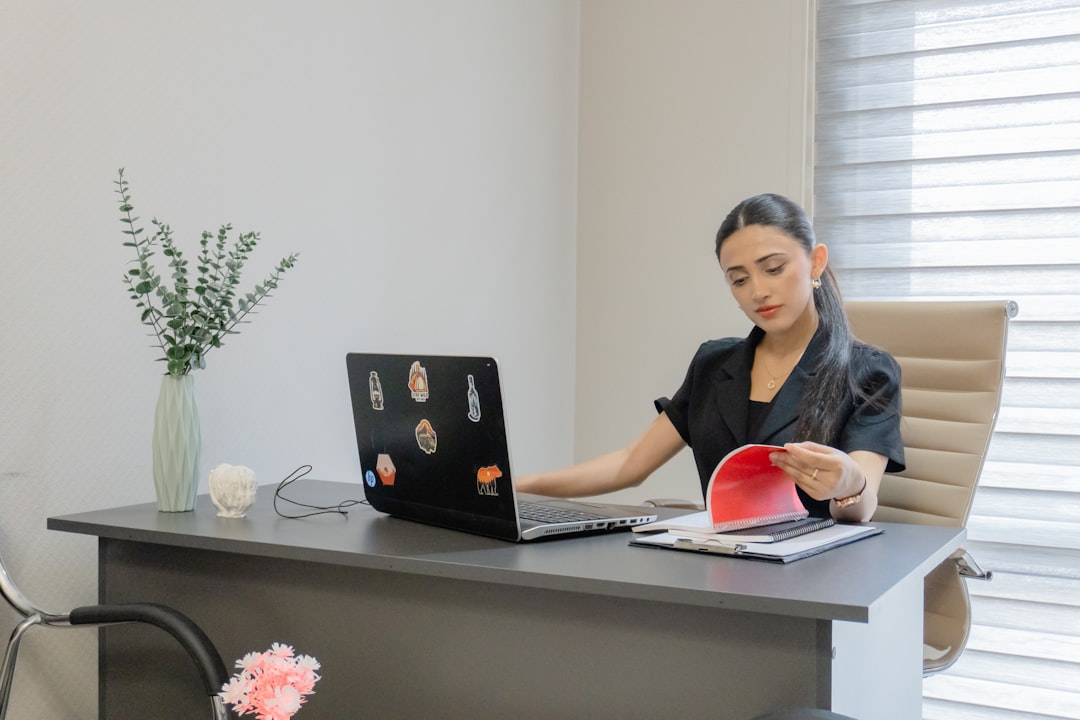 Woman working on laptop and reading papers at desk.